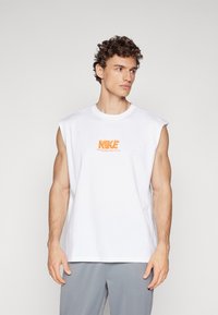 Witte mouwloze T-shirt van katoen. Voorzien van een oranje Nike-logo met de tekst "OVERWINNING BEHOORT TOT ONS." Gladde textuur, casual pasvorm.