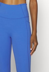 Modré legíny s vysokým pasem vyrobené z elastického materiálu s hladkou strukturou, se zdobnými švy a boční kapsou.