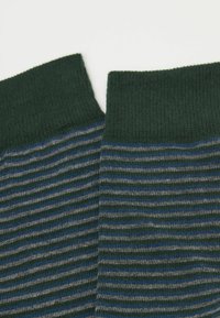 Grüne Socken mit einem gerippten Bündchen, die horizontale Streifen in Grau und Blau aufweisen. Weicher Stoff mit einer Farbverbindung.