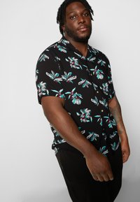 Short-sleeve black shirt with white and turquoise floral pattern, button-up design, and a relaxed fit.