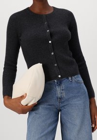 Cardigan gris foncé à côtes avec cinq boutons, associé à une pochette de couleur claire, porté sur un jean en denim bleu.