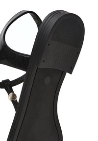 Semelle de sandale noire avec grip texturé et bride de cheville dotée d'une boucle argentée, vue de dessous.