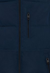 Mörkblå pufferjacka med hel dragkedja, två dragkedjefickor och en quiltad textur, designad för värme och komfort.