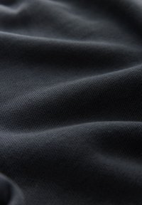 Gros plan de la texture d'un tissu noir montrant un motif tricoté fin et des plis doux créant des vagues ombrées.