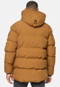Brun pufferjakke med hætte, med en quiltet design, justerbar halsrem og sort detalje på skulderen.