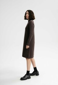 Braunes langärmliges Kleid mit geradem Schnitt, gestrickter Textur und runder Ausschnit, kombiniert mit schwarzen Schuhen und Socken.