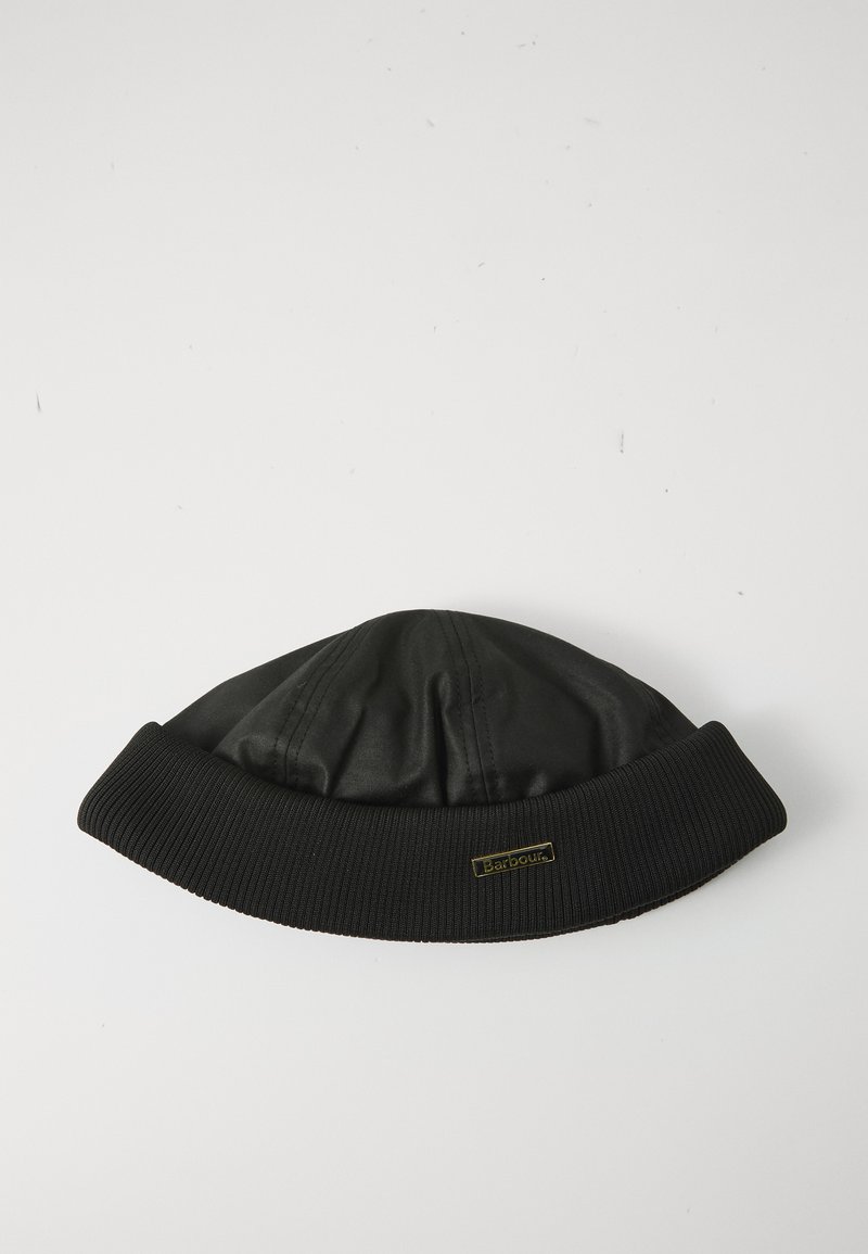 Gorro preto Barbour com aba dobrada canelada e pequeno emblema dourado em fundo branco liso.