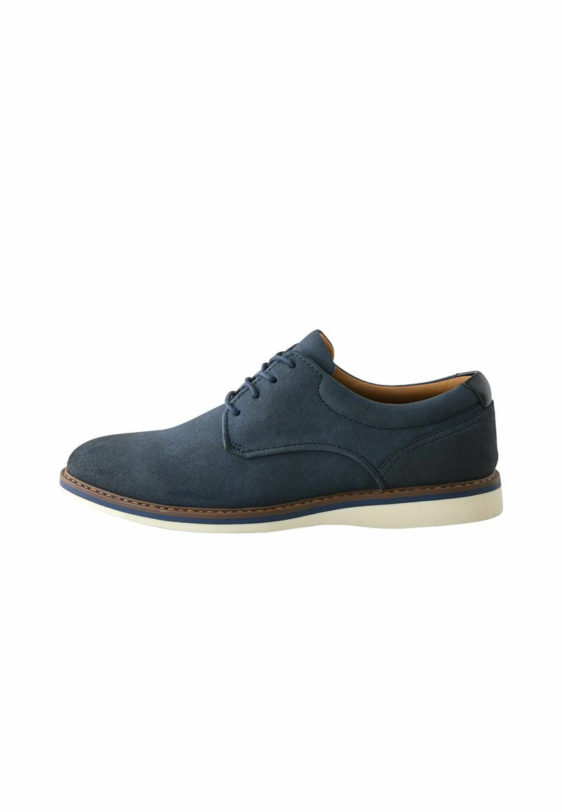 Chaussure en daim bleu marine avec une texture lisse, bout arrondi et semelle en caoutchouc blanche. Présente une fermeture à lacets et des détails de couture contrastants.