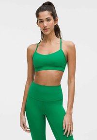 Groene sportbeha met dunne bandjes, gladde textuur en een aansluitend ontwerp, gecombineerd met hoge groene leggings met een naadloze afwerking.