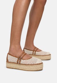 Geflochtene Espadrilles mit Plattformsohle aus natürlichen Fasern, cremefarbenem Obermaterial, braunen Lederriemen und runder Zehenform.