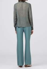 Blusa verde trasparente con un motivo geometrico, abbinata a pantaloni plissettati color turchese. I dettagli notevoli includono maniche lunghe e una vestibilità comoda.