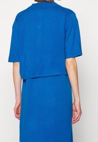 Skuren blå stickad tröja med krage, korta ärmar och en texturerad tyg, kombinerad med en matchande blå klänning. Slät allmän utseende.