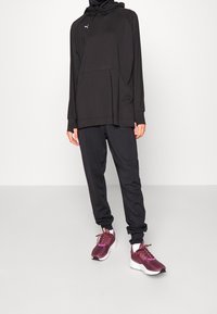 Svart atletisk hoodie med dragsko och framfickor, kombinerad med matchande svarta joggers. Avslutad med vinröda sneakers med vita sulor.