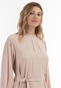 Rochie roz deschis cu mâneci lungi, textură strânsă la umeri, guler cu volane și o curea din material la talie. Material neted.