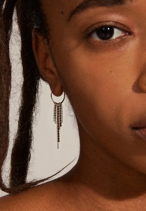 Boucles d'oreilles en argent en forme de créole avec plusieurs chaînes pendantes de longueurs variées, conçues pour les femmes. Gros plan sur l'oreille d'un modèle.