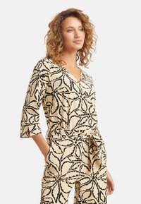 Romper met bloemenpatroon in roomwit en zwart, met een V-hals, driekwart mouwen en een ceintuur in de taille voor een relaxte pasvorm.