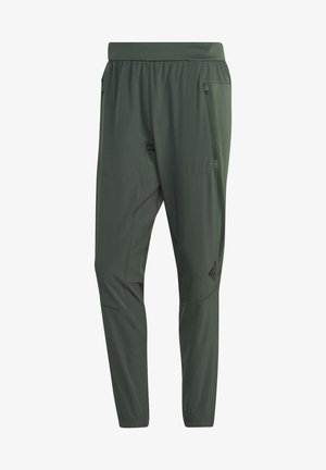 Persona con camiseta sin mangas negra, pantalones verdes y zapatillas negras saltando la cuerda sobre fondo blanco.