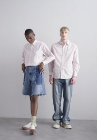 Rosa stripete skjorte med knapper, denimskjørt med frynser, og blå jeans; uformelt fottøy; nøytral bakgrunn.