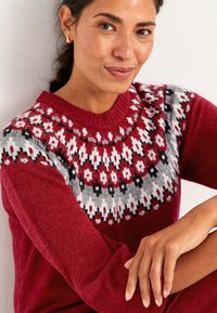 Rød strikket sweater med et mønstret skærf i grå, hvid og sort. Har ribbet halsudskæring og lange ærmer. Blød tekstur.