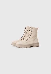 Botas de tobillo beige de ante con suela de goma, que cuentan con cordones redondos, ojetes de metal y una suela texturizada y gruesa.