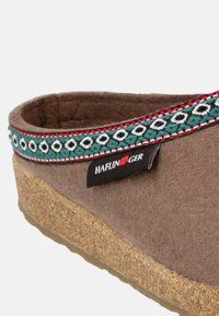 Scarpa slip-on in felt marrone con suola in sughero, caratterizzata da una fascia ricamata colorata con dettagli verdi, bianchi e rossi. Etichetta del marchio visibile.