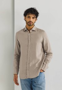Helles beige Leinenhemd mit schmalem Kragen, langen Ärmeln und passenden Knöpfen, kombiniert mit blauen Jeans.