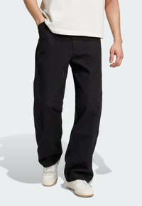 Svarta cargobyxor med lös passform, tillverkade av robust tyg, med sidofickor och synliga sömmar, i kombination med vita sneakers.