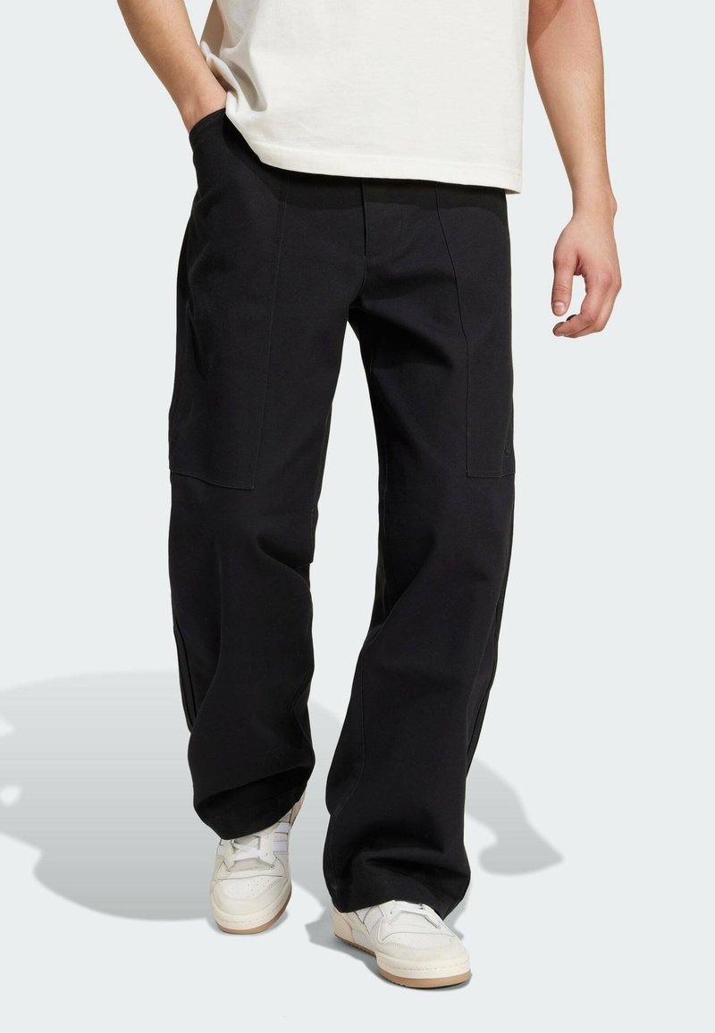 Svarta cargobyxor med lös passform, tillverkade av robust tyg, med sidofickor och synliga sömmar, i kombination med vita sneakers.