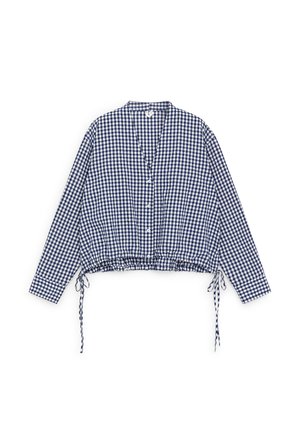 Blauw-witte geruite blouse met lange mouwen, knoopsluiting aan de voorkant en trekkoord aan de zoom, plat neergelegd op een witte achtergrond.