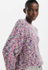 Textúrájú, oversized pasztell rózsaszín pulóver, multiszínű pöttyökkel. Kerek nyakú és leengedett vállú, puha fonalból készült.