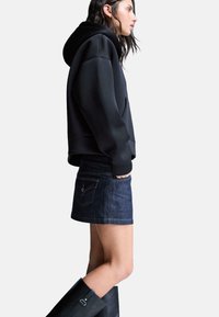 Zwarte hoodie, denim mini rok, hoge zwarte laarzen. De hoodie heeft een losse pasvorm en de rok heeft achterzakken met stiksels.