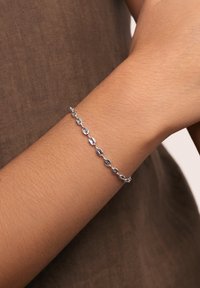 Bracciale in argento su un polso, con anelli ovali dalle superfici lucide e una chiusura sicura. Colore della pelle visibile sotto.