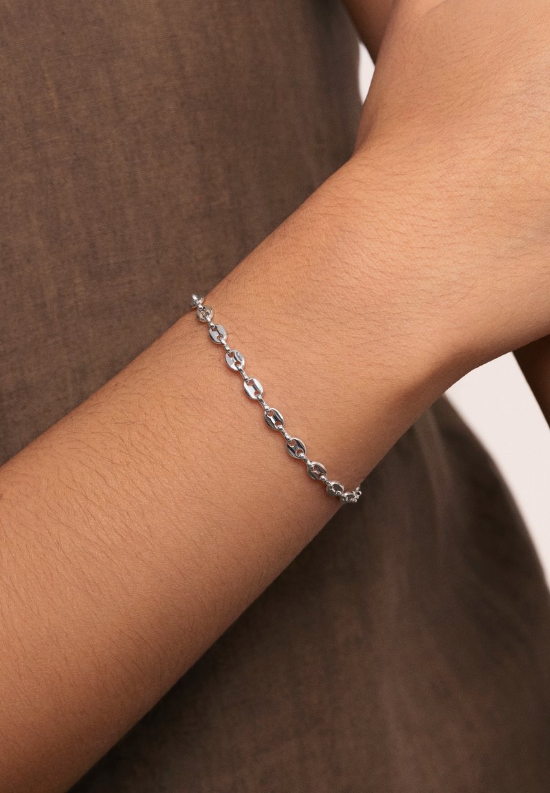 Bracciale in argento su un polso, con anelli ovali dalle superfici lucide e una chiusura sicura. Colore della pelle visibile sotto.