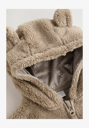 Hanorac din fleece bej, cu o textură moale, urechi de urs și un interior căptușit cu un model discret de puncte. Închidere cu fermoar în față.