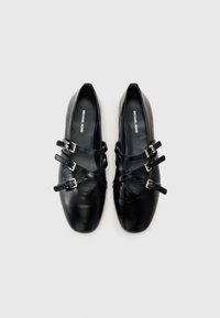 Black leather shoes with a rounded toe, featuring multiple crossed straps and buckles for secure fastening. Smooth texture, minimalist design.