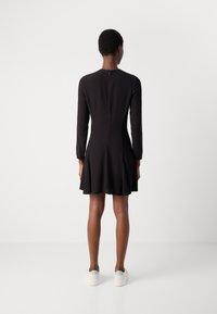 Melna kleita ar garām piedurknēm un izplūdušu svārku, ar rāvējslēdzēju aizmugurē. Apvienota ar gaišiem sporta apaviem. Gluda tekstūra.