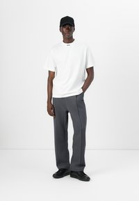 Tricou alb cu mânecă scurtă și logo-ul "BOSS" pe guler, asociat cu pantaloni gri cu croi drept și pantofi negri. Design minimalist.