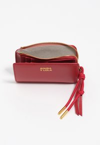 Czerwony skórzany portfel z złotym zamkiem, otwarty, z beżową materiałową wyściółką, frędzlem ze złotymi końcówkami oraz wytłoczonym na złoto napisem "BIMBA Y LOLA" z przodu.