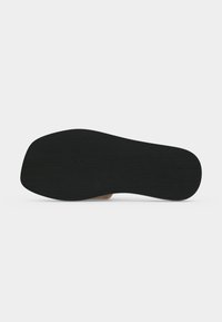 Semelle de chaussure noire avec un talon plat, surface lisse et texture subtile, montrée de dessous sur fond blanc.