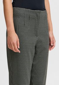 Pantalons à motifs pied-de-poule noir et blanc avec une coupe ajustée, présentant une texture de tissu lisse et une taille mi-haute.