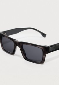 Óculos de sol com armação de padrão tartaruga escura, lentes cinzentas e detalhes pretos brilhantes nas hastes, apresentando formato quadrado e hastes grossas.