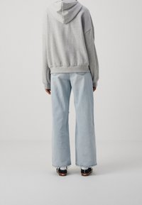 Šedá mikina s kapucí a spadlými rameny, kombinovaná s světle modrými širokými džínami s opranými okraji a černými teniskami.