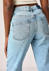 Jeans de mezclilla azul claro con cintura media, diseño de cinco bolsillos y un ligero desvanecimiento. La tela tiene una textura de sarga clásica.