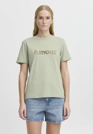 Light green short-sleeve T-shirt with a round neckline, featuring embroidered "Amour" in a textured design. Paired with blue denim shorts.