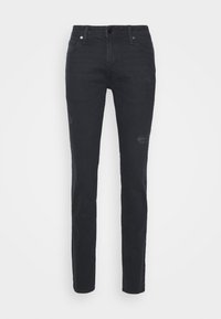 Jeans de mezclilla negros ajustados con parches descoloridos y ligero desgaste. Bolsillos frontales y cierre de botón y cremallera en la parte delantera.