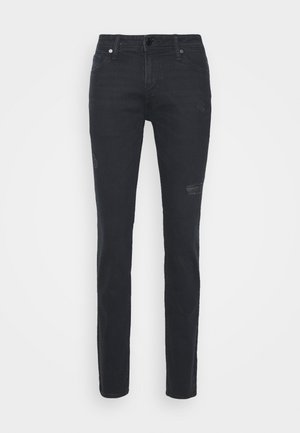 Jeans de mezclilla negros ajustados con parches descoloridos y ligero desgaste. Bolsillos frontales y cierre de botón y cremallera en la parte delantera.