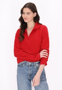 Rød fleece-pullover med kvartziipperkrave, lange ærmer og en blød tekstur, parret med lyseblå højtaljede jeans.