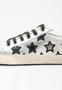 Metalické stříbrné tenisky se zelenými tkaničkami, zdobené barevnými výšivkami hvězd v modré, černé a stříbrné na svršku. Gumová podešev.