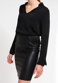 Maglietta nera a maniche lunghe con scollo a V e colletto, abbinata a una gonna in pelle nera aderente con accenti rigati sui lati.