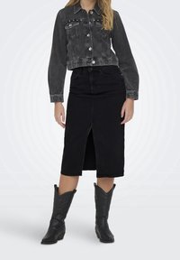 Svart kort jeansjacka med knappstängning, kombinerad med en knälång svart jeanskjol med sprund fram, kompletterad med svarta cowboystövlar.